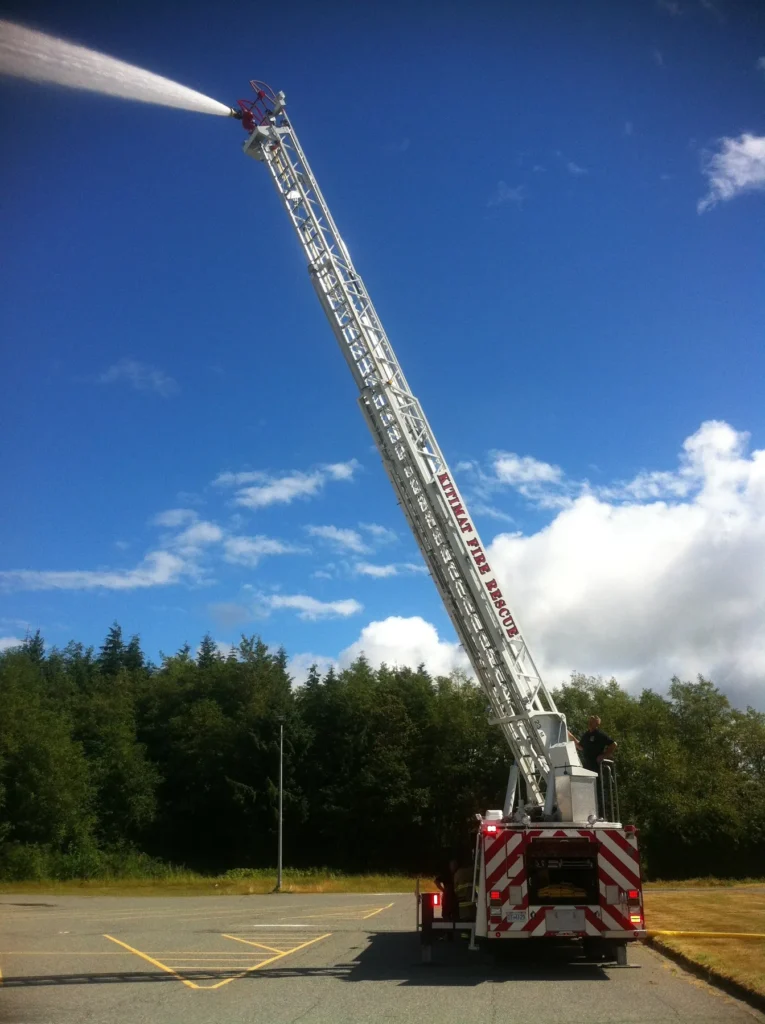 Kitimat Fire Rescue aerial ladder flowing a master stream against a blue sky