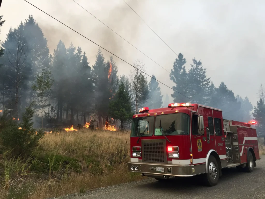 Kitimat fire engine working a wildfire, with flames in the dry grass beside the road